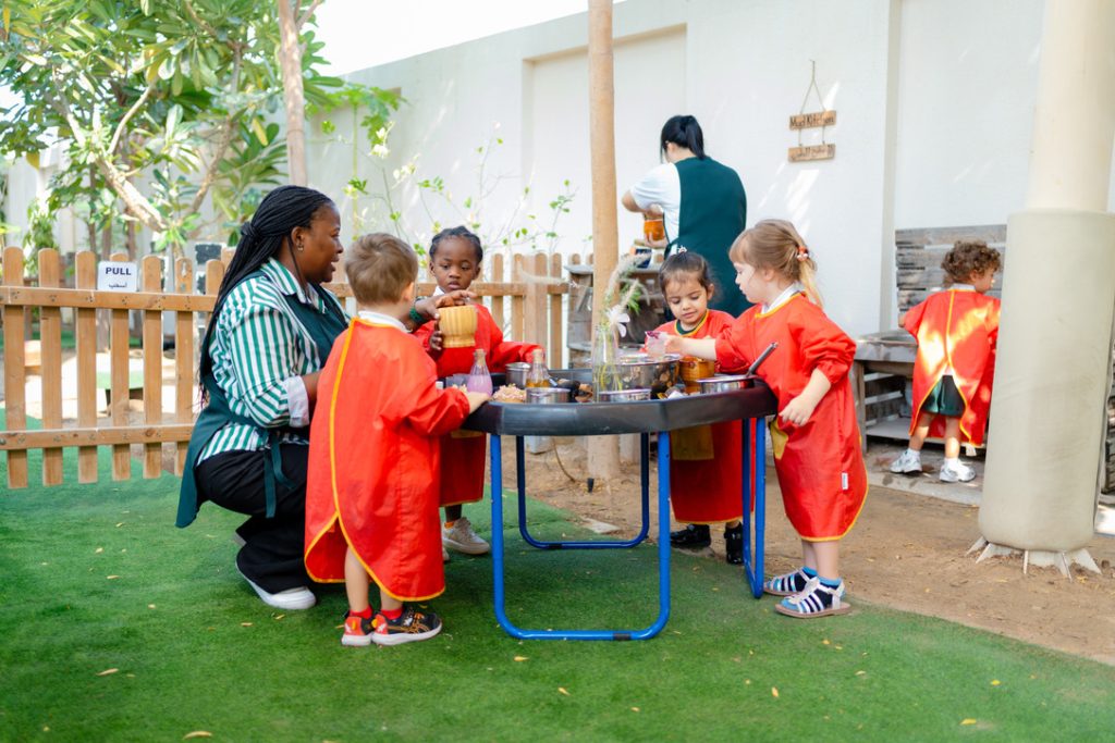 Young children and teacher doing outdoor sensory play activity supporting EYFS learning and development